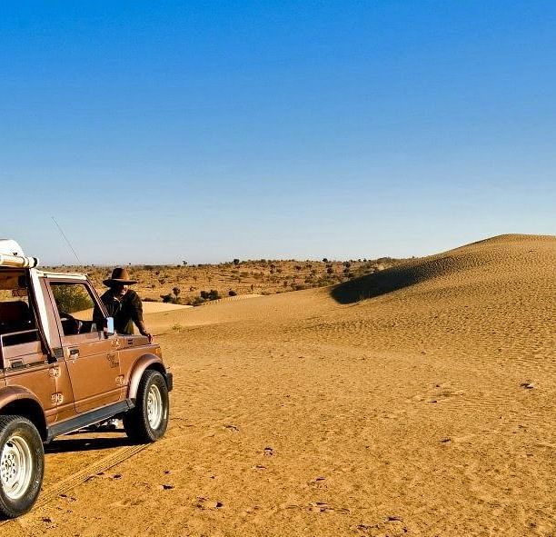 An image of a desert campsite featuring a jeep with a rugged desert landscape and sparse vegetation surrounding it at Manvar Resort & Desert Camp