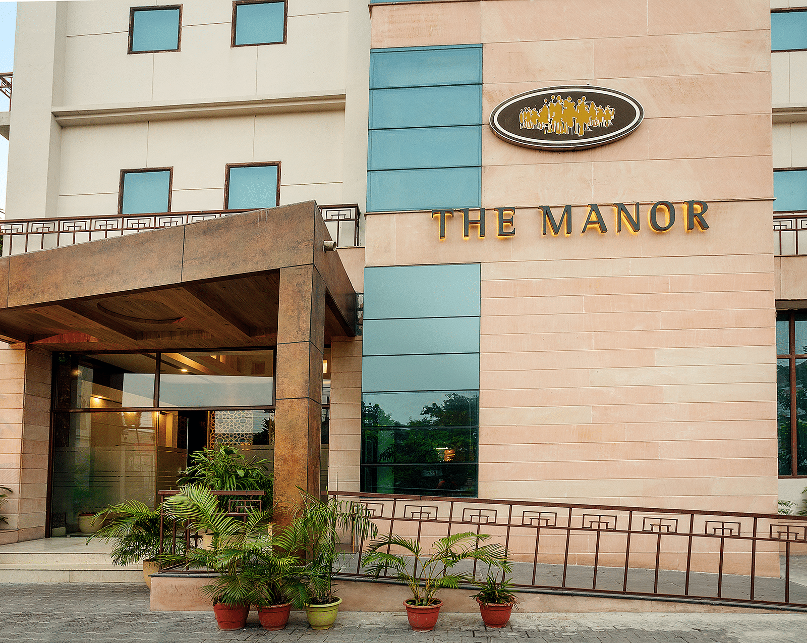 facade image of The Manor hotel, showcasing a modern entrance with potted plants and a clear blue sky above - The Manor, Bareilly