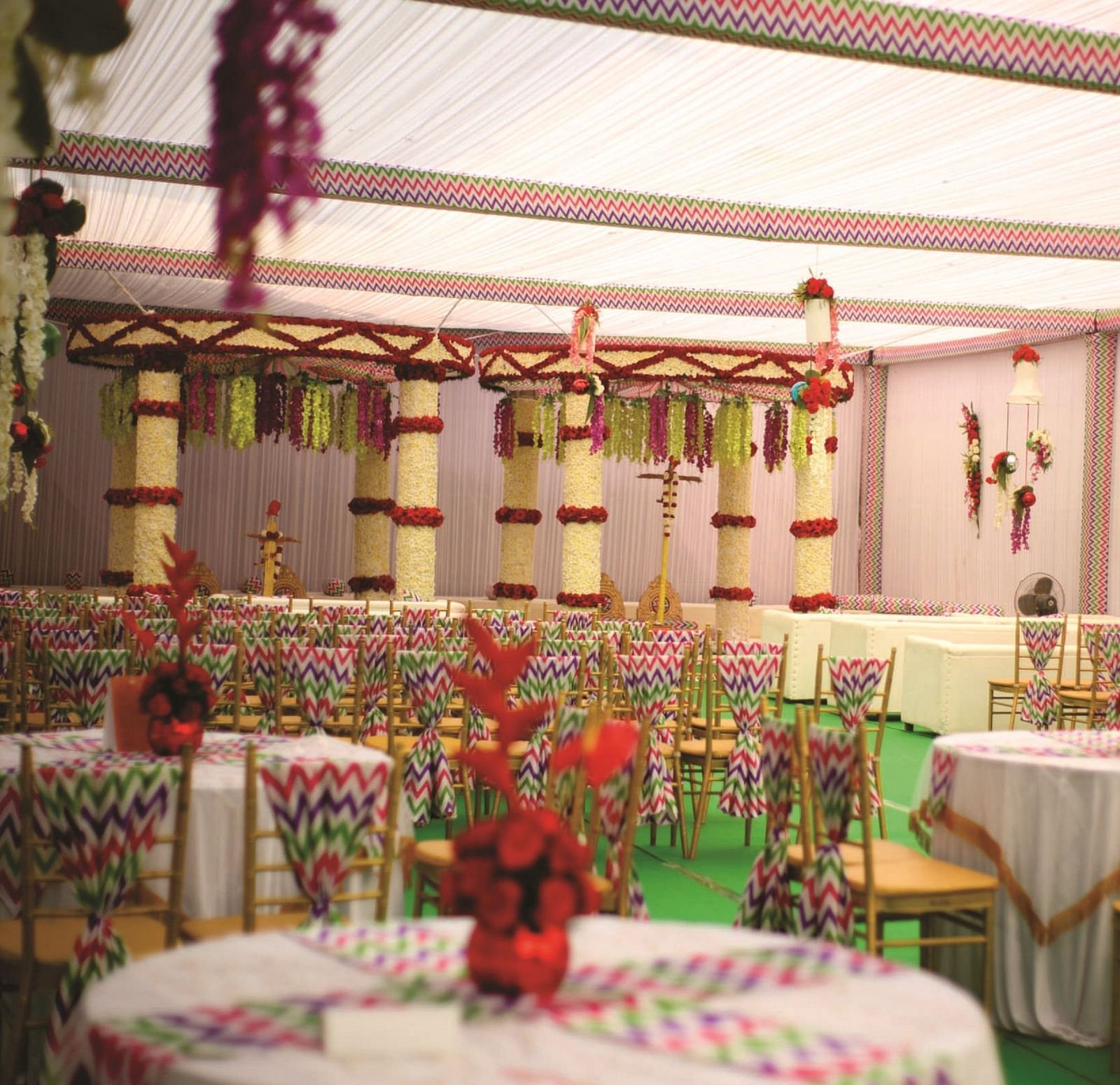 A wedding setup with vibrant floral decorations and round tables with chairs | Gemini Continental