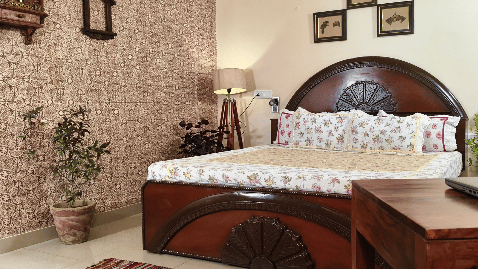 A bedroom with a double bed, wooden desk, potted plants and framed pictures on the wall at Jaypore360 Homestay in Jaipur.