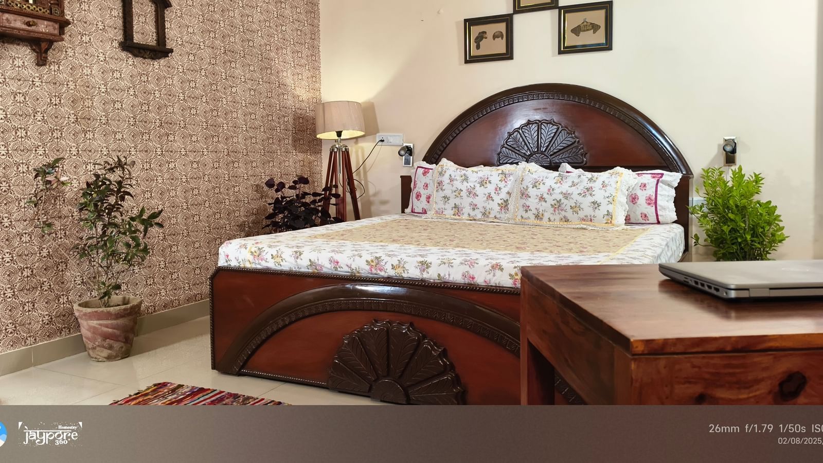 A bedroom with a double bed, wooden desk, potted plants and framed pictures on the wall at Jaypore360 Homestay in Jaipur.