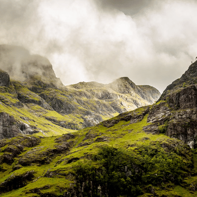A landscape of steep, rocky mountains covered in green grass, with low-hanging clouds obscuring the peaks.