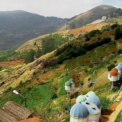 A panoramic shot of a hill station with colourful houses scattered on terraced hills, overlooking misty mountains.