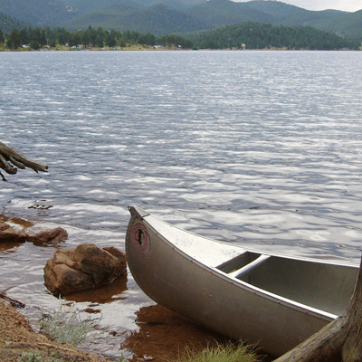 A lakeside view with a boat docked near the shore, surrounded by greenery and distant hills in the background.