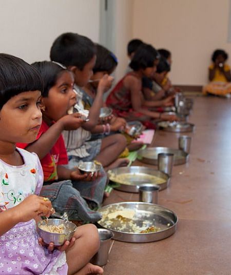 People eating from plates on the floor, indoor setting - Shreyas Retreat