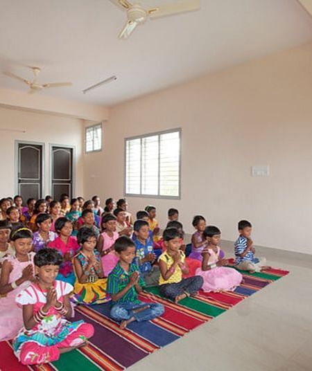 People and children, sitting on mats, working on projects, indoor setting - Shreyas Retreat