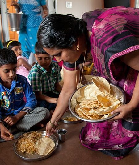 People eating from plates on the floor, indoor setting - Shreyas Retreat