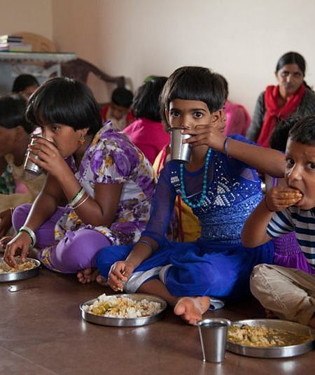Children, sitting on the floor eating from plates, indoor setting - Shreyas Retreat