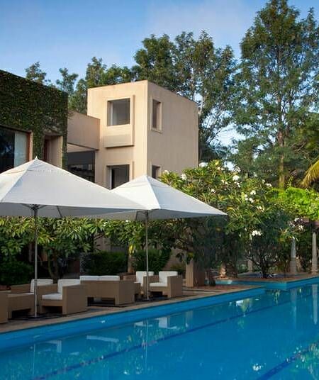 A swimming pool with lounge chairs and a building with a white umbrella, outdoor setting - Shreyas Retreat