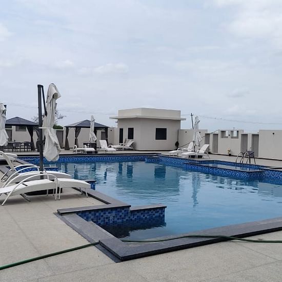 Rooftop swimming pool with tiled edges, surrounded by lounge chairs and closed umbrellas; cabanas in the background and a hose lying across the pool deck in the foreground under a partly cloudy sky - Kyriad Prestige, Ilkal