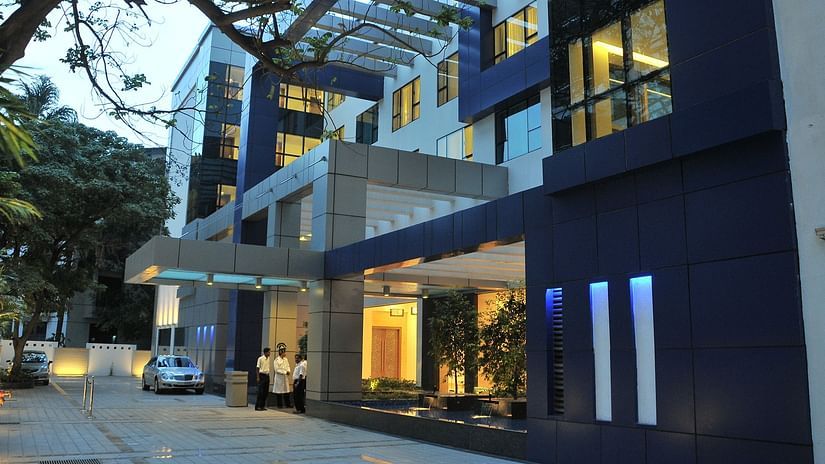 The exterior of a modern, multi-story building with blue and grey accents, illuminated at dusk - Adarsh Hamilton.