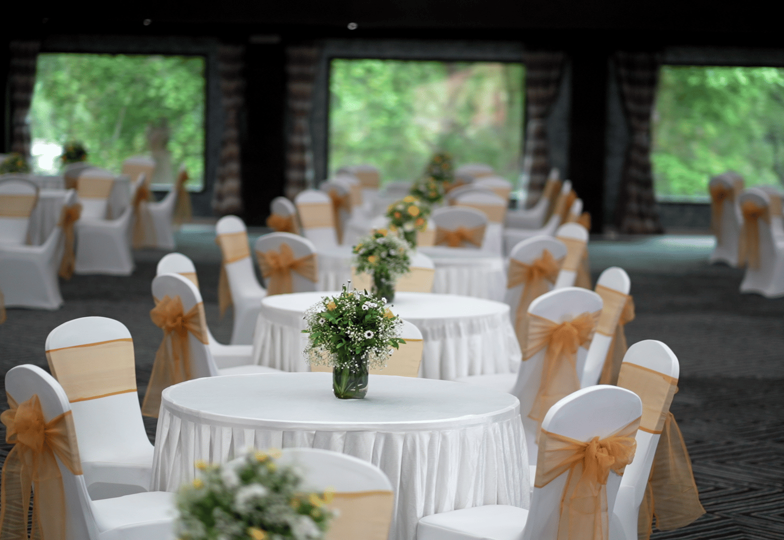 Banquet hall setup with round tables, white and gold chair covers, and floral centrepieces at Narayani Heights Hotel & Resorts, Ahmedabad.