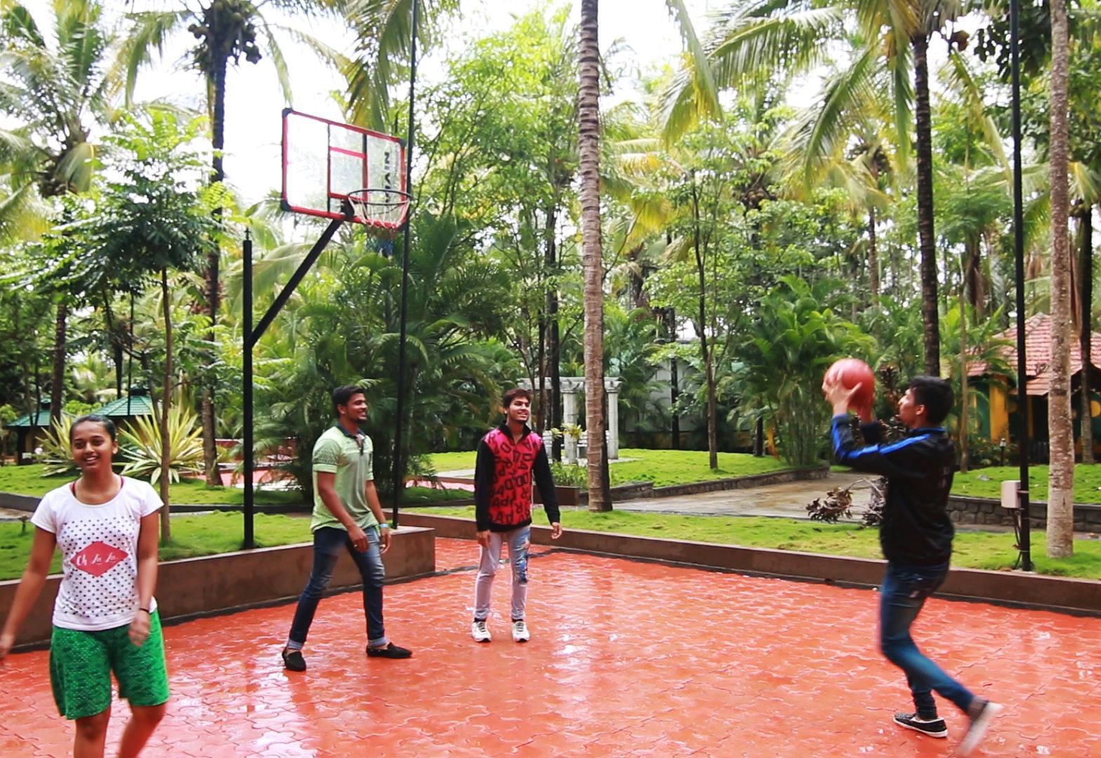 Image of four people playing basketball with trees in the background at Parampara Resort & Spa, Kushalnagar.