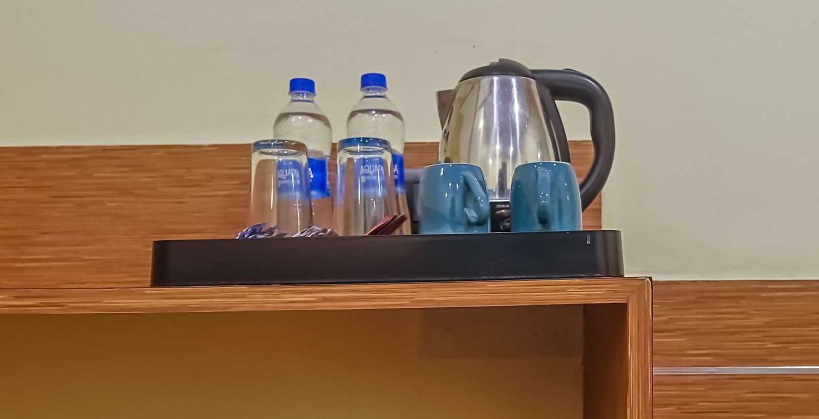 Shelf with water bottles, kettle, cups and digital safe at Max Hotel Prayagraj.
