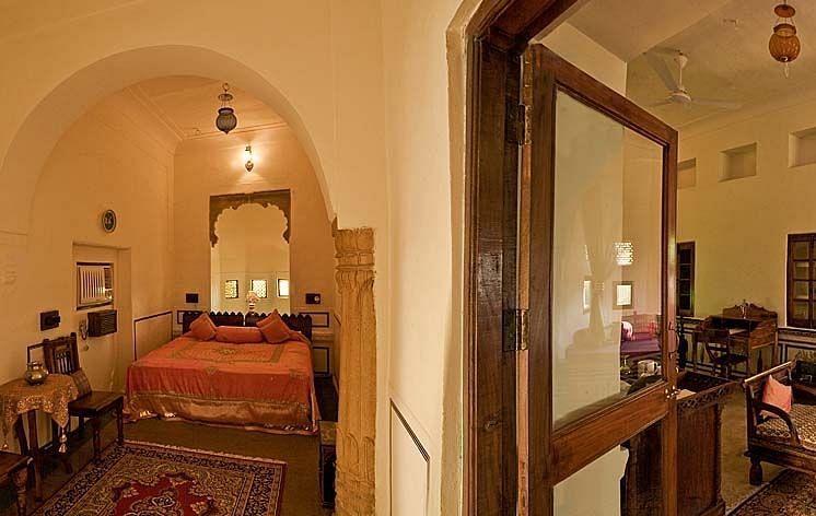 A panoramic view of an elegantly furnished suite at Fort Barli, showcasing arched doorways, a plush bed, and a cosy seating area.