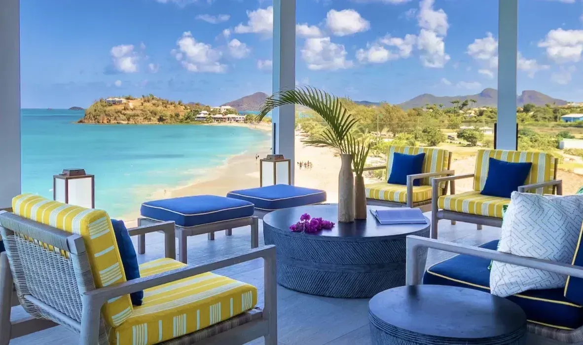 A spacious living area with modern furniture, featuring expansive windows overlooking a vibrant blue ocean and a distant island.