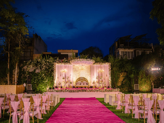 The Brij Nest Lawn featuring a floral stage, aisle seating, ambient lighting, and landscaped surroundings prepared for an evening celebration | Clarks Amer, Jaipur