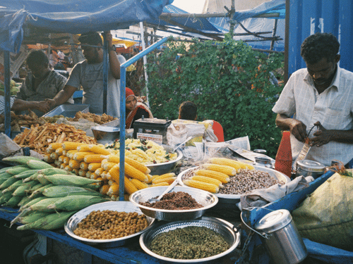 Street food vendor at a covered market stall filled with fresh corn and spices.