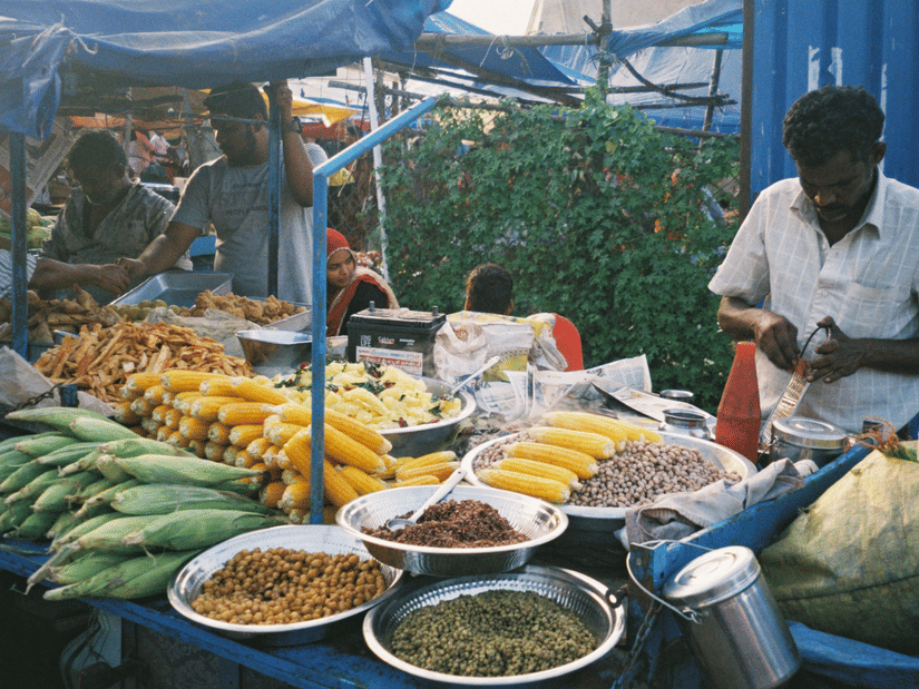 Street food vendor at a covered market stall filled with fresh corn and spices.