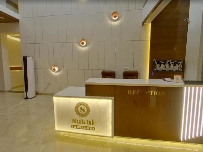 Reception area with a wooden desk featuring an illuminated logo, set against a backdrop of textured walls and ambient lighting.- Sukhi - A Luxury Stay Inn, Chikkamagaluru