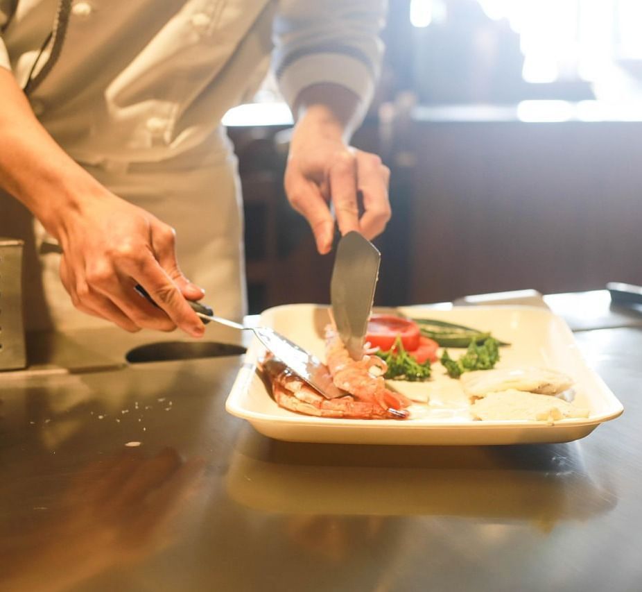 A chef placing shrimps on a white porcelain plate with the help of spatulas.