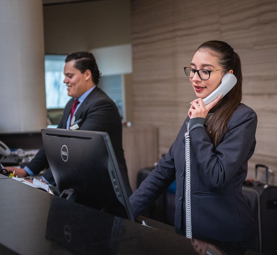 2 staff members standing behind the reception desk with desktops in front of them.