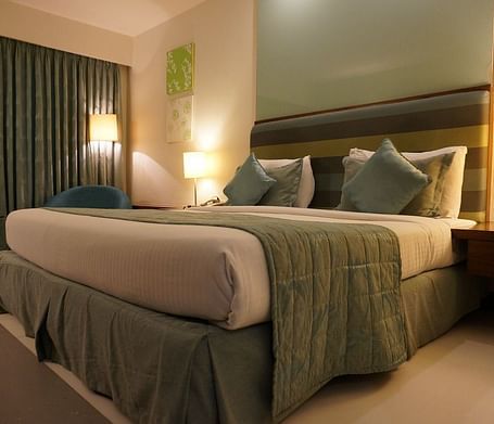 A double bed with pillows and cushions kept neatly against the head board of the bed in a warmly lit room.