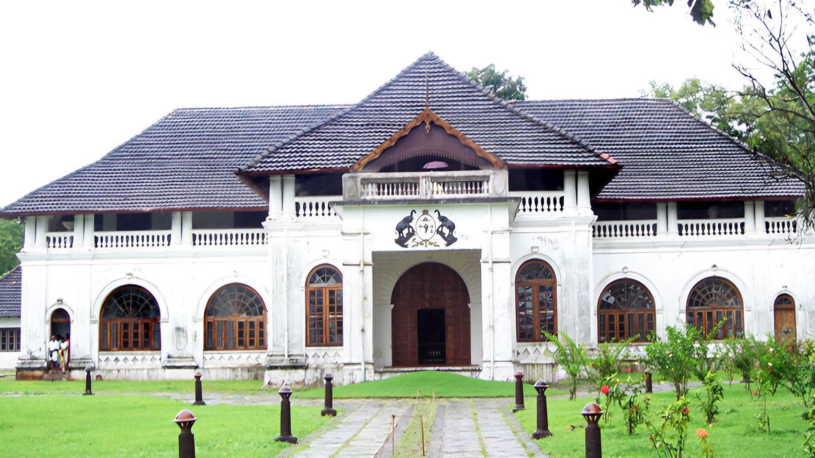 Mattancherry Palace with sloping tiled roof, white walls, and green lawn in front.