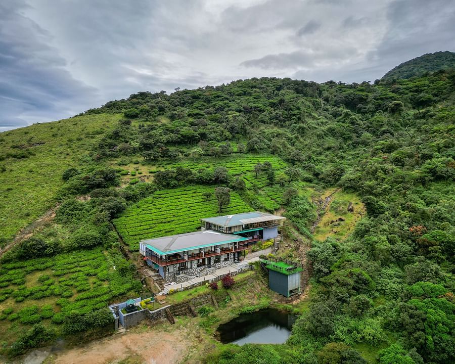 An aerial shot of the the resort surrounded by greenery and mountains on all sides and clear sky in the background | Ibex Stays and Trails