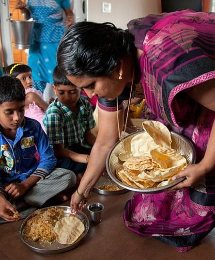 People eating from plates on the floor, indoor setting - Shreyas Retreat