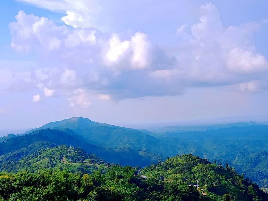 An overview of lush green mountains with white clouds on blue sky in the background.