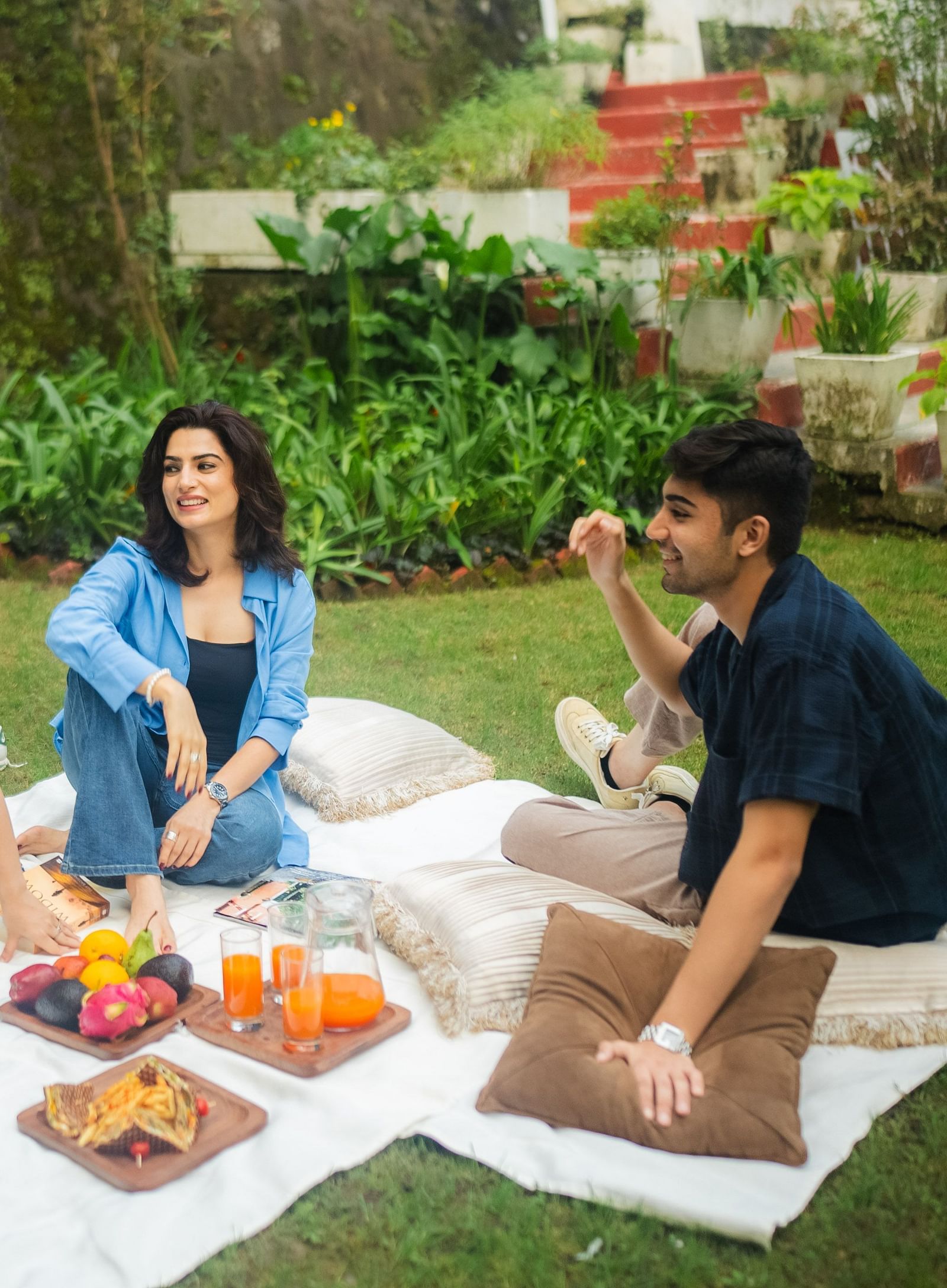 A family having a picnic on a blanket spread on lawn, enjoying a relaxed outdoor gathering with snacks and drinks.