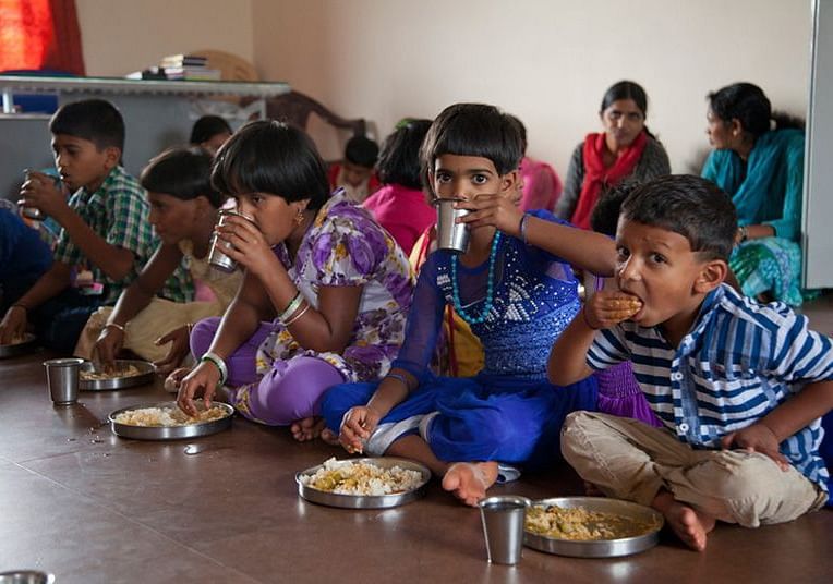 Children, sitting on the floor eating from plates, indoor setting - Shreyas Retreat