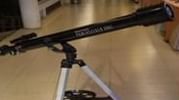A black telescope is mounted on a tripod indoors