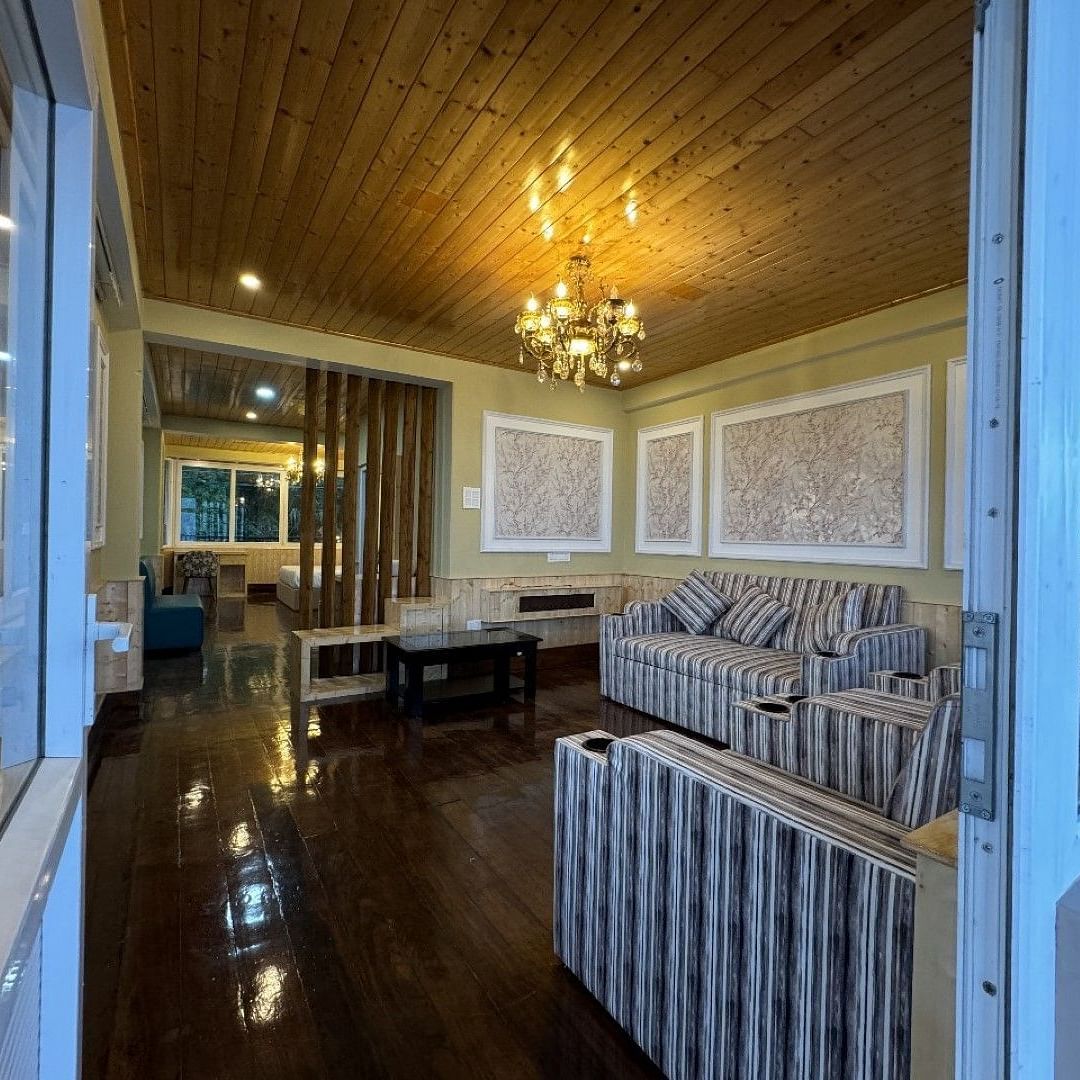 An image of a seating room which has a seating area like sofa, centre table. Chandelier hung from a wooden ceiling - Avianna Group of Hotels & Resorts