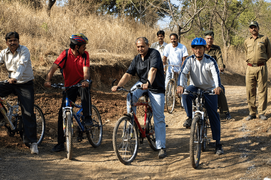 A group of people riding bicycles along a dirt trail in a rural outdoor setting accompanied by a guide standing nearby.