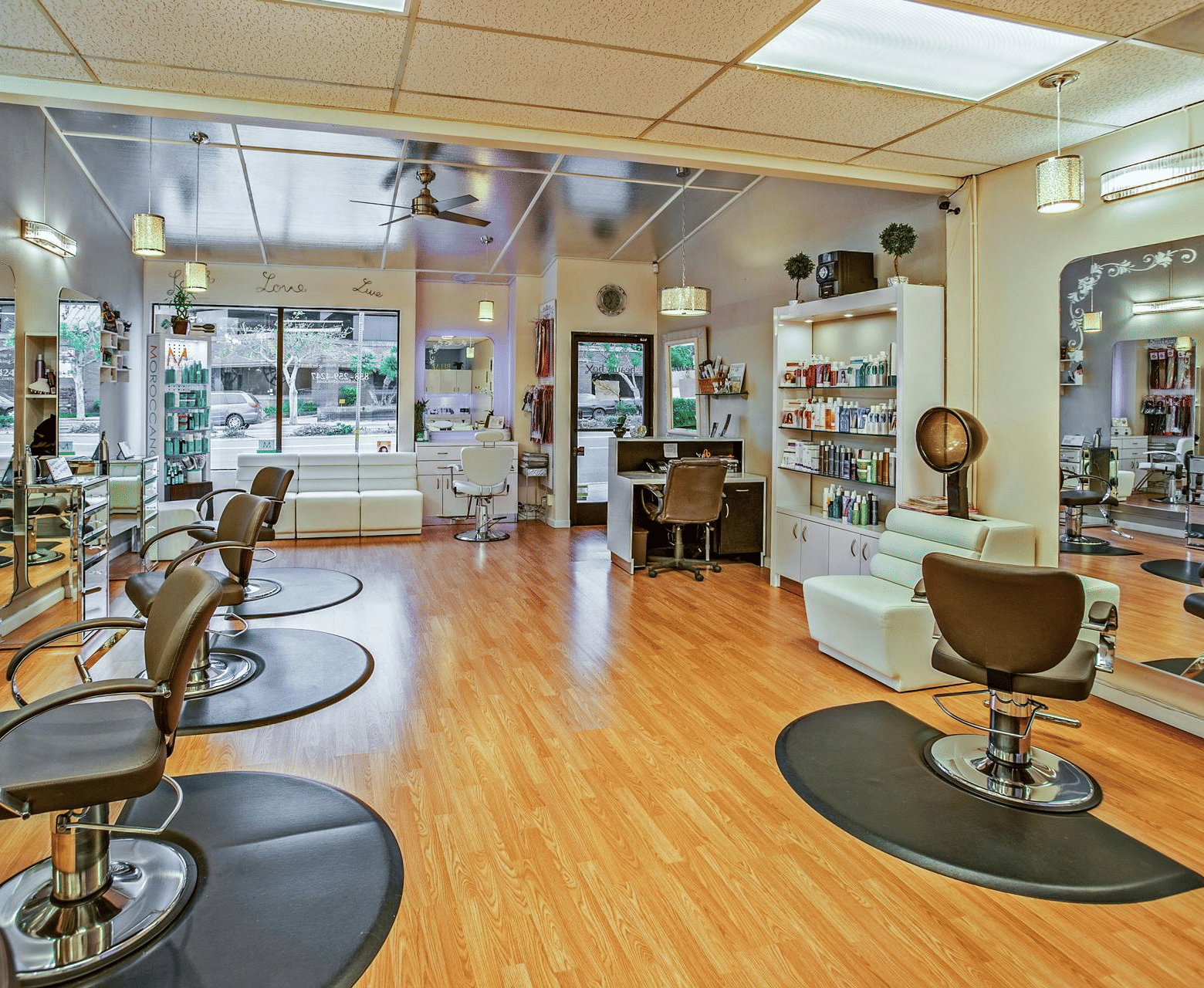The bright, contemporary interior of a hair salon with wooden flooring, several styling chairs, and products displayed on shelves.