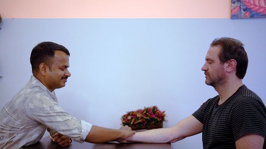 Two men shake hands across a table, engaged in a greeting or agreement.