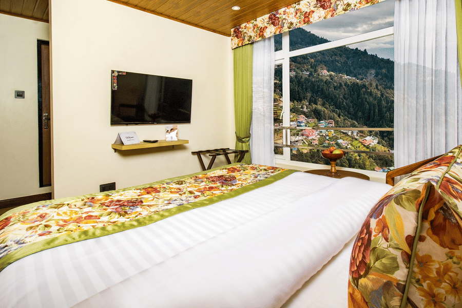 Cosy hotel room in Darjeeling featuring large windows overlooking forested hills and colourful mountain-side homes | Mount Lungta Boutique Hotel & Spa