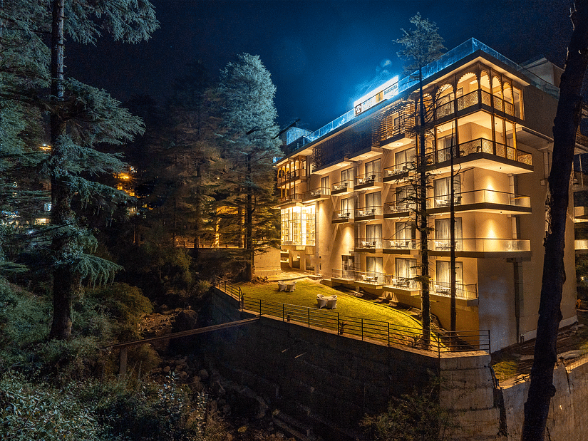 A hotel building illuminated at night, nestled amidst lush greenery.