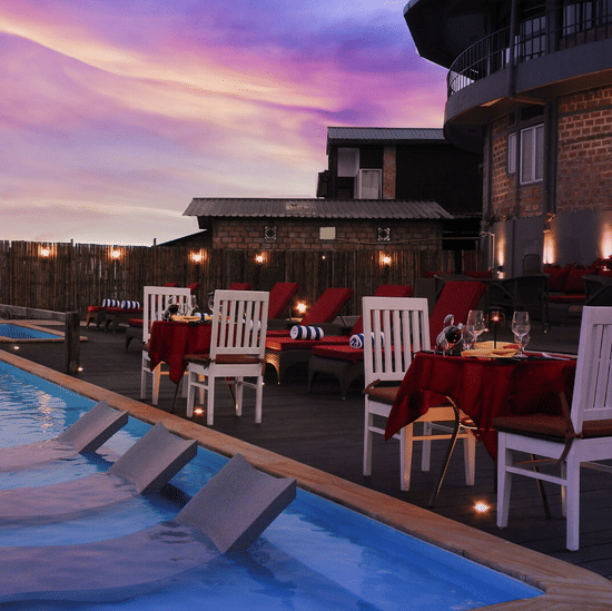 Poolside dining setup with white chairs and red-draped tables beside the swimming pool under a pink sunset sky at Polo Resort Cherrapunji.