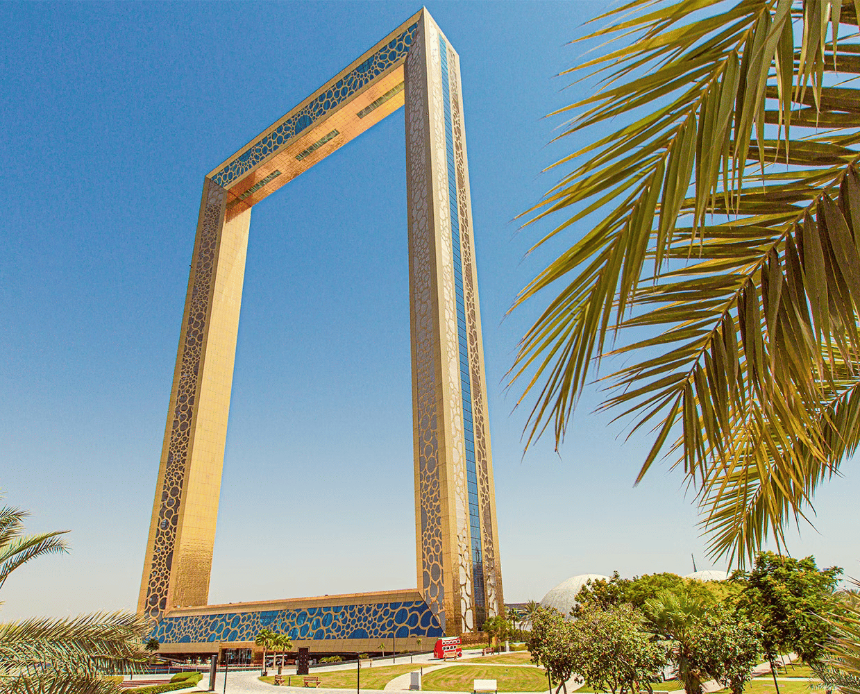 The large, gold rectangular monument of Dubai Frame stands tall against a clear sky, framing the surrounding city landscape.