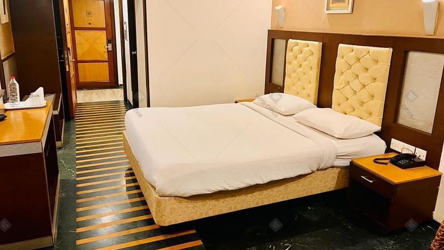 A bedroom with warm lighting, queen-size bed, telephone placed on the side table and classic furnishings at Hotel Dr Rajkumar International.