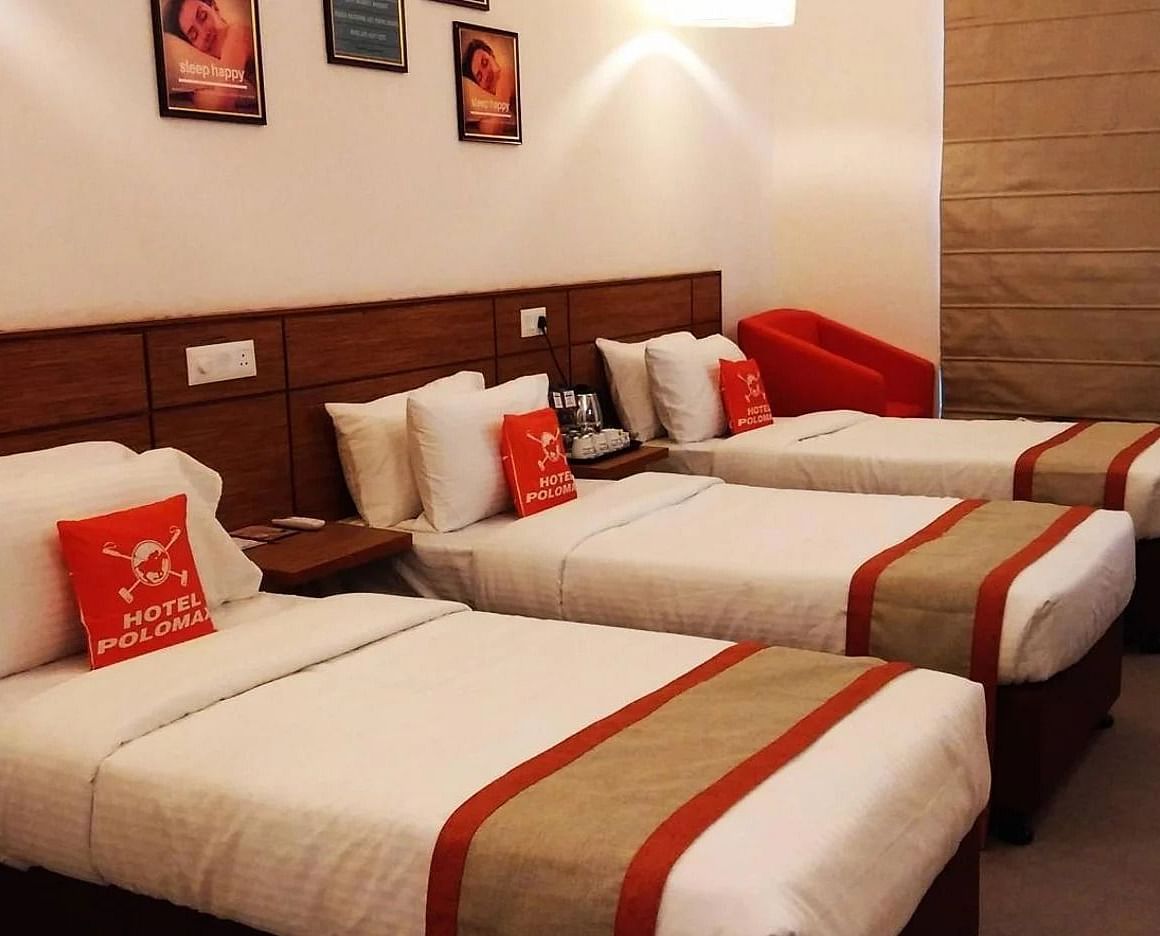 A room featuring three single beds with white linens and brown and red accents at Max Hotel Jabalpur.