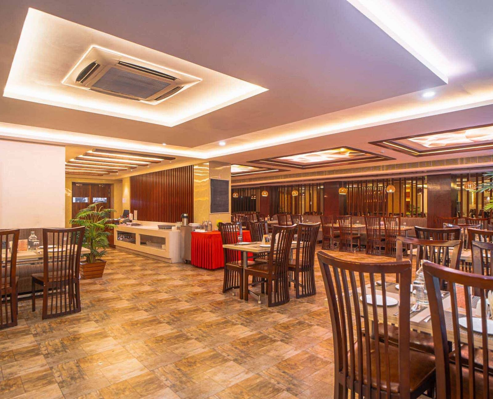 A wide shot of a spacious dining area with wooden tables and chairs, illuminated by warm ceiling lights at Mansha Hotel Regency.