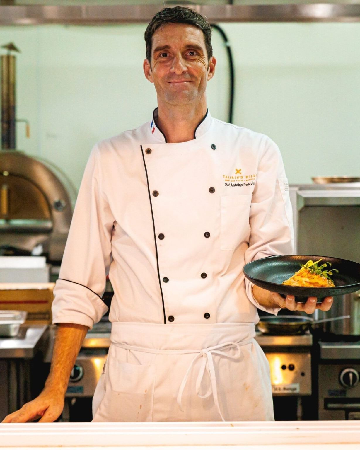 Chef standing in a Tamarind Hills Antigua – Resort & Villas restaurant kitchen holding a dish of grilled vegetables