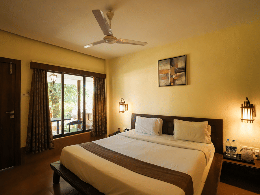 A well-appointed bedroom at Adamo The Village featuring a large bed, window seating, and warm ambient lighting.