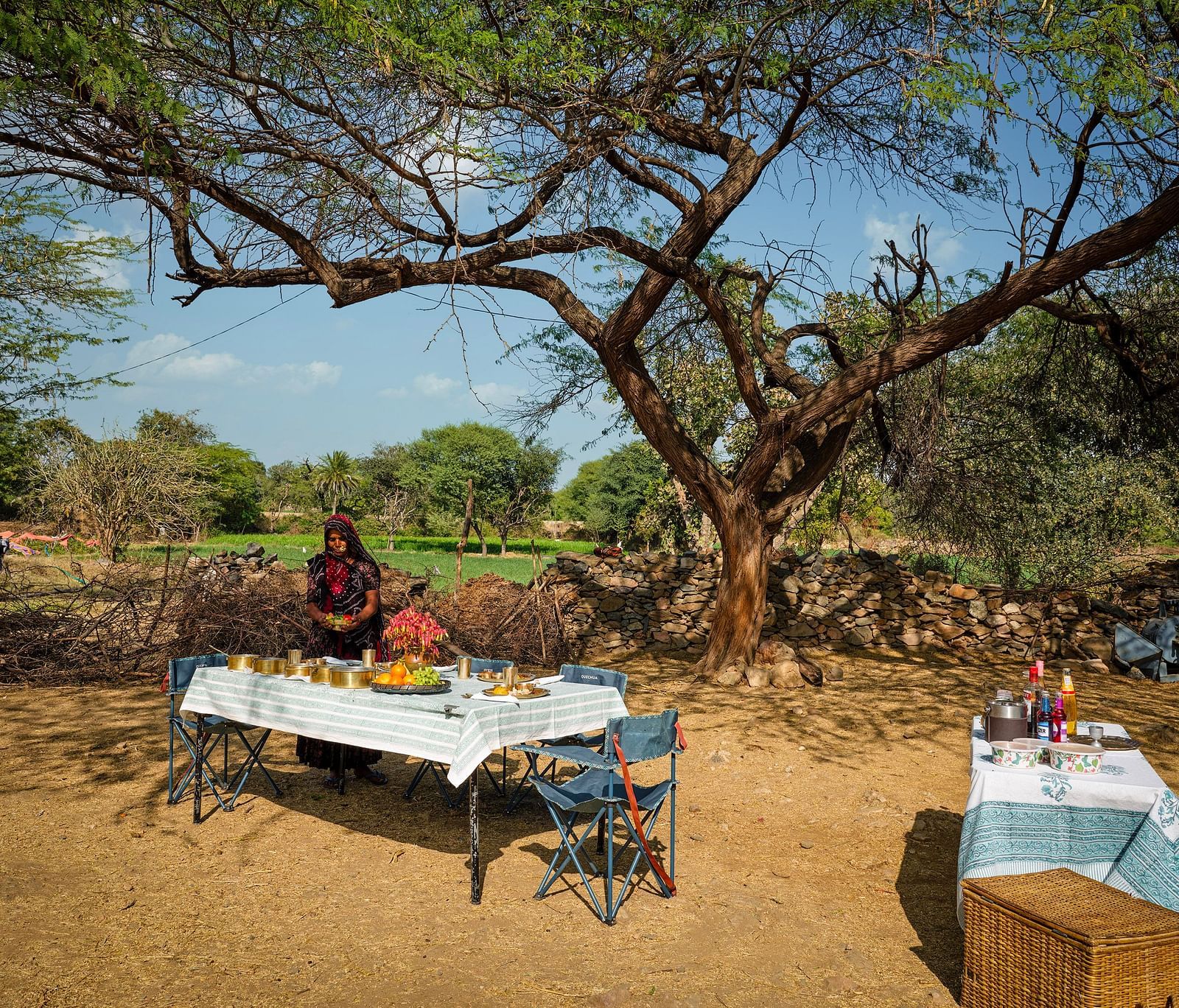 image of a woman dressed in traditional outfit serving various rajasthani delicacies on the table at dev shree, deogarh