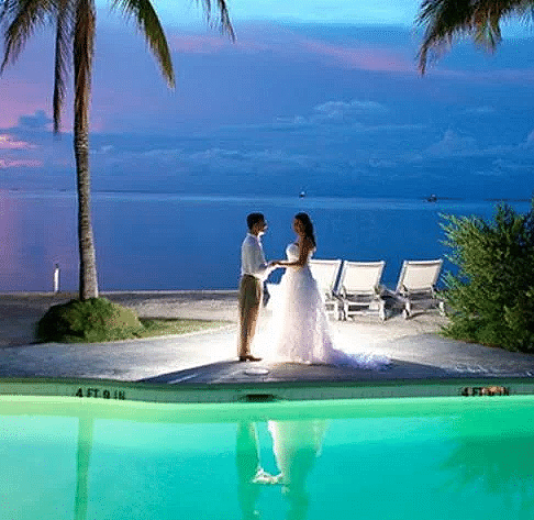 A couple stands near the poolside at Casa Morada with lounge chairs and palm trees in the background during sunset.