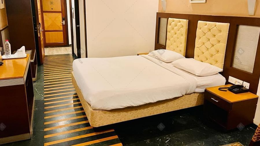 A bedroom with warm lighting, queen-size bed, telephone placed on the side table and classic furnishings at Hotel Dr Rajkumar International.